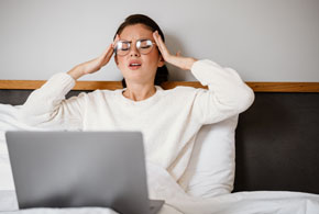 Stressed young woman with laptop computer in bed